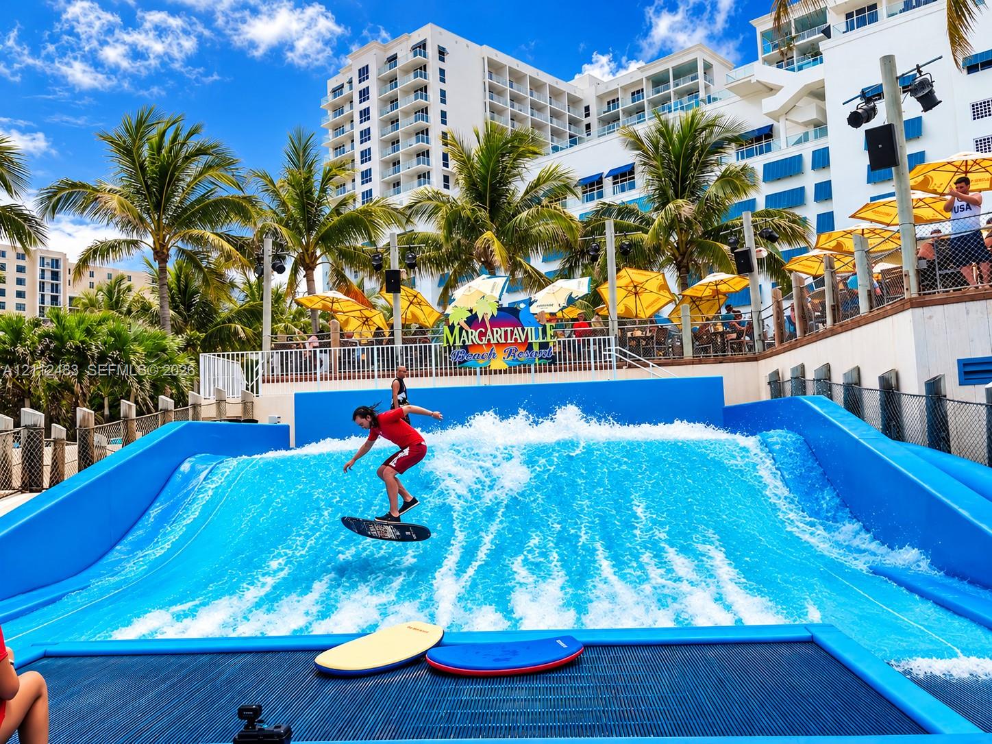 Surfing wave simulator featuring a high-pressure water system, tiered spectator decking, and perimeter security fencing