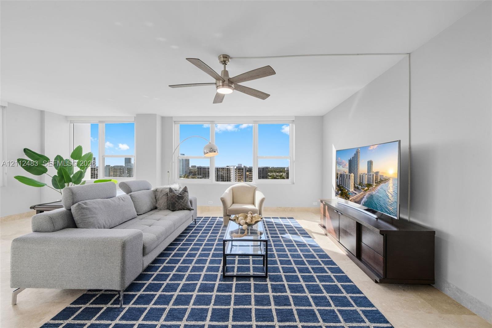 Open-concept living space featuring large-format tile flooring, expansive floor-to-ceiling windows, integrated ceiling fan with light fixture, and skyline city scenery