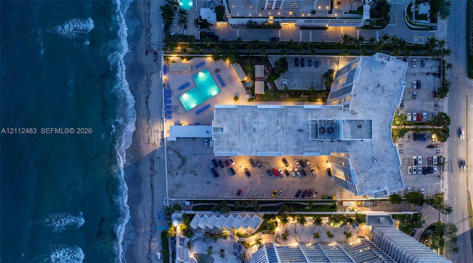 Aerial perspective of an oceanfront property featuring a swimming pool, direct shoreline access, and surface parking