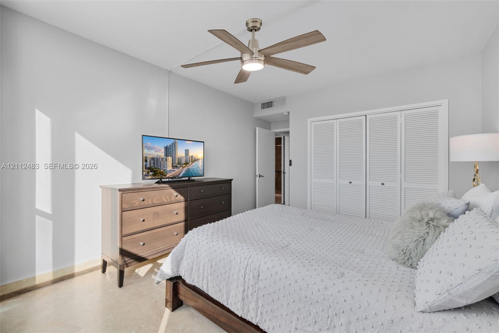 Room featuring neutral-toned walls, polished concrete flooring, a multi-blade ceiling fan with integrated lighting, and white louvered-panel closet doors