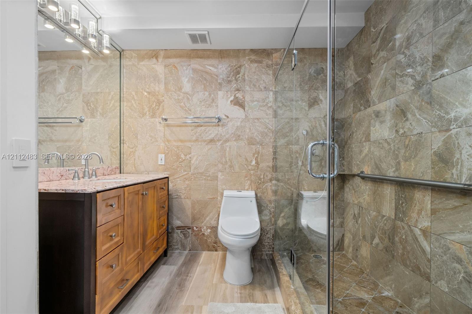 Bathroom featuring stone-tile wall finishes, wood-finish cabinetry with a stone countertop, a glass-enclosed shower, and a polished-chrome light fixture