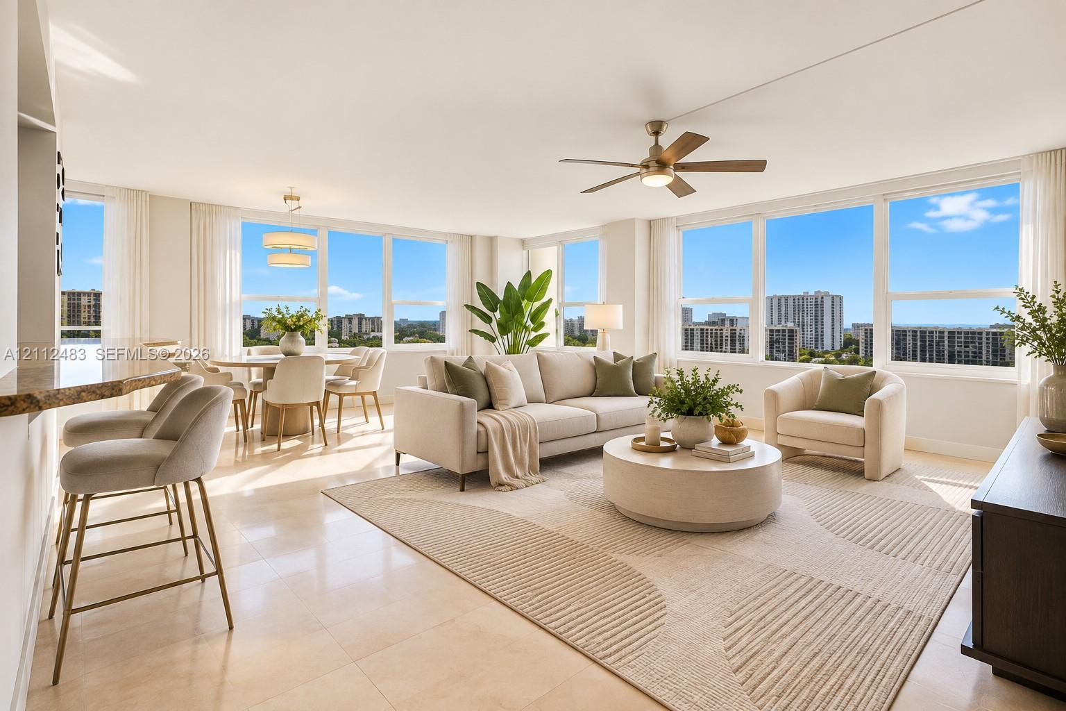 Open-concept interior featuring large-format stone flooring, expansive floor-to-ceiling windows, integrated breakfast bar with stone countertop, multi-blade ceiling fan, and tiered modern chandelier