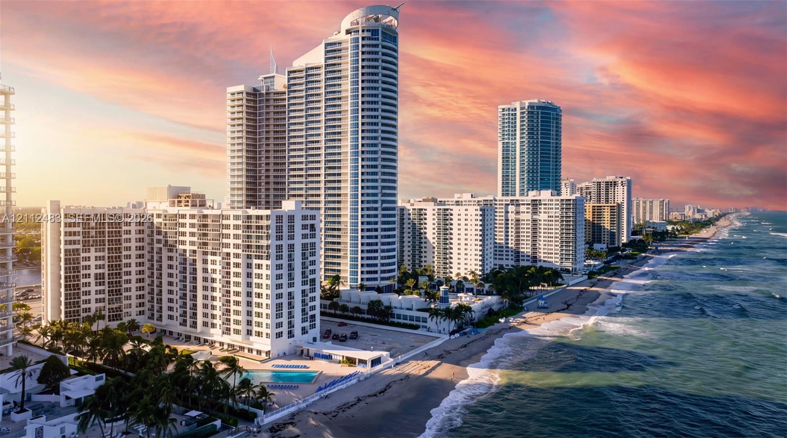 High-rise residential tower exterior featuring direct oceanfront access, balcony terraces, a ground-level swimming pool, and tropical landscaping