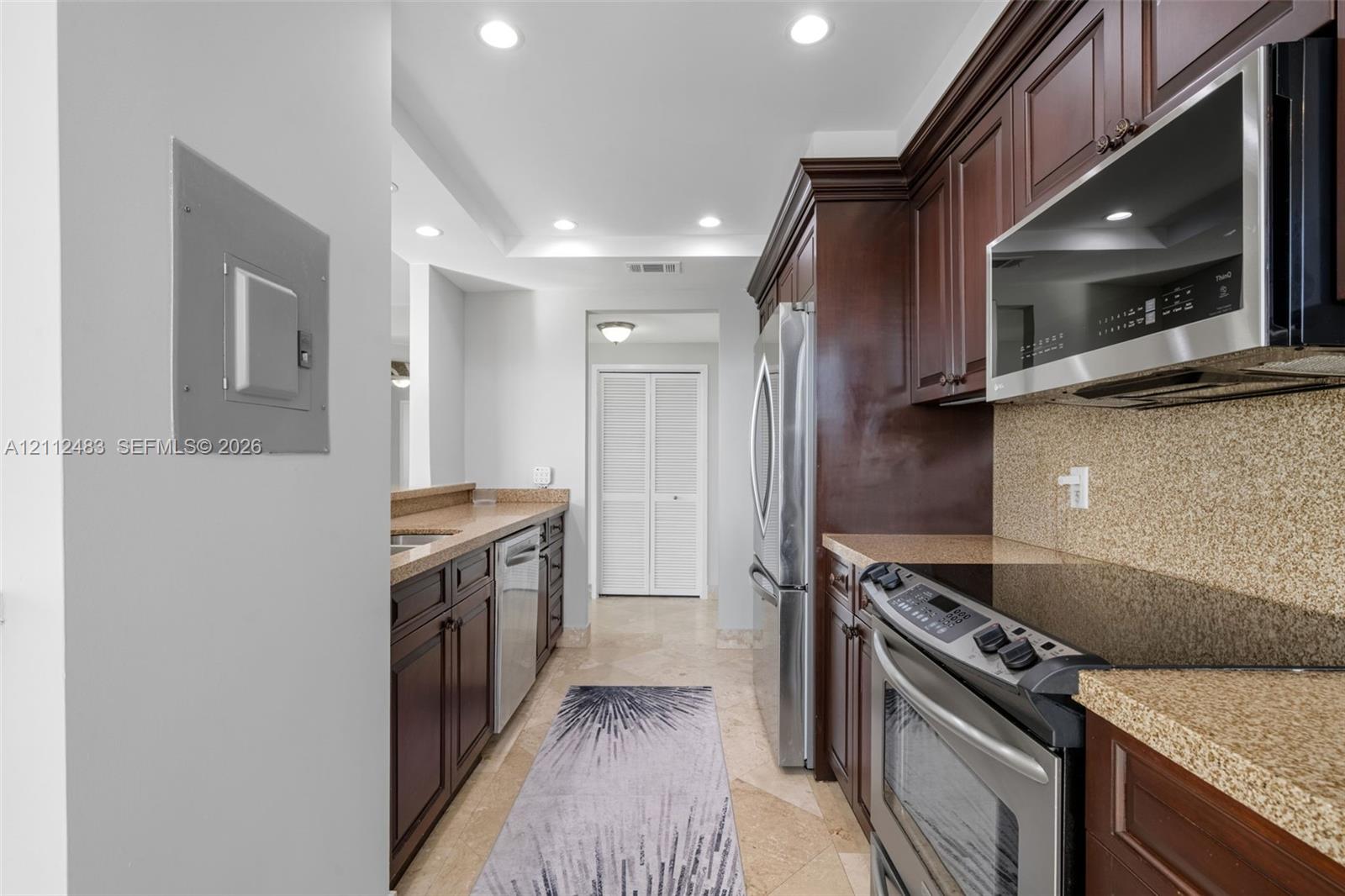 Kitchen featuring dark wood cabinetry, stone countertops, stainless steel appliances, and stone flooring