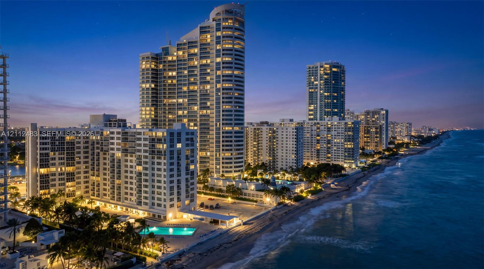 High-rise residential tower featuring glass-facade architecture, direct oceanfront positioning, ground-level swimming pool, and manicured palm tree landscaping