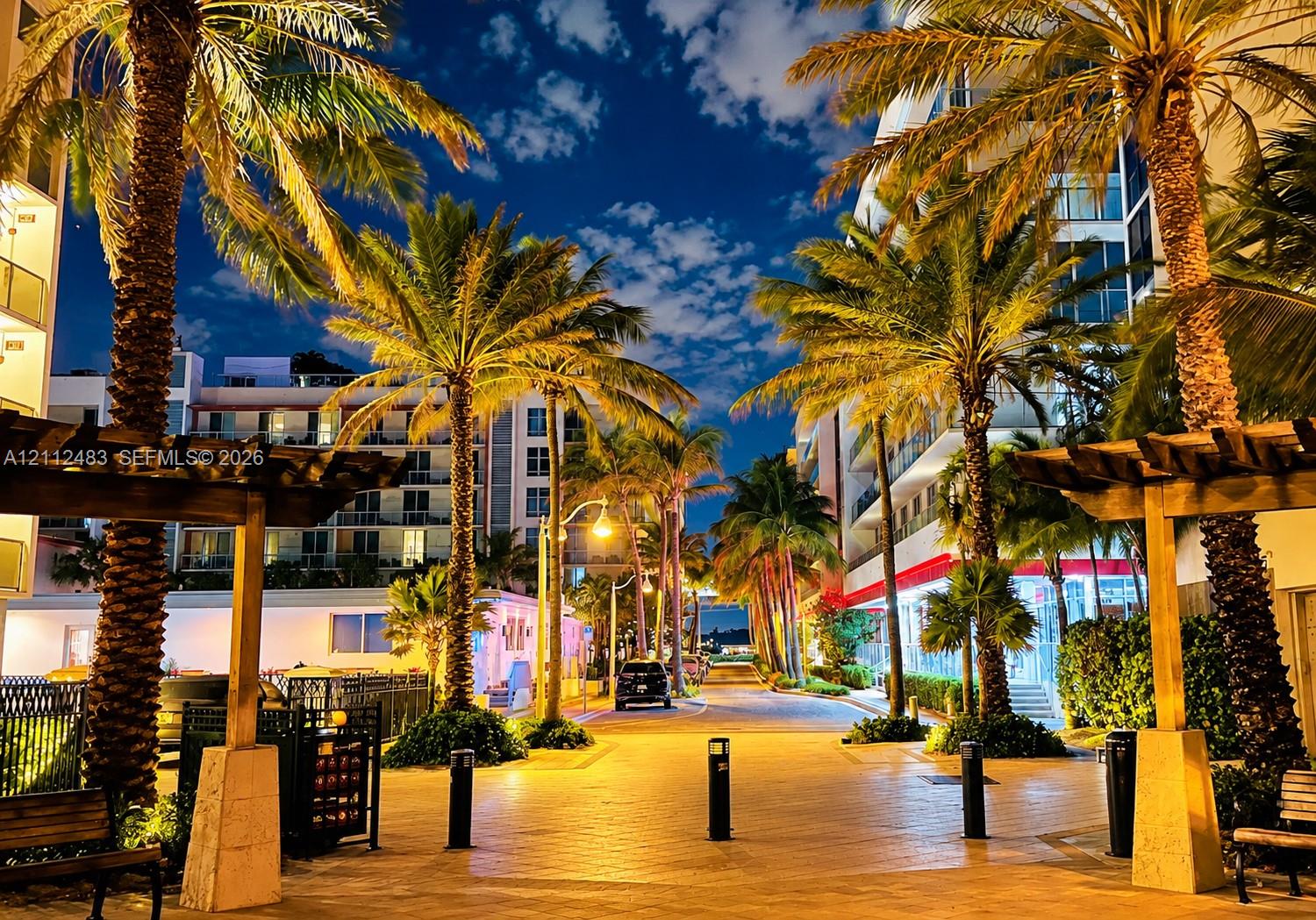 Exterior pedestrian walkway featuring stone-paved paths, wood-frame pergolas, mature palm trees, and modern multi-story structures