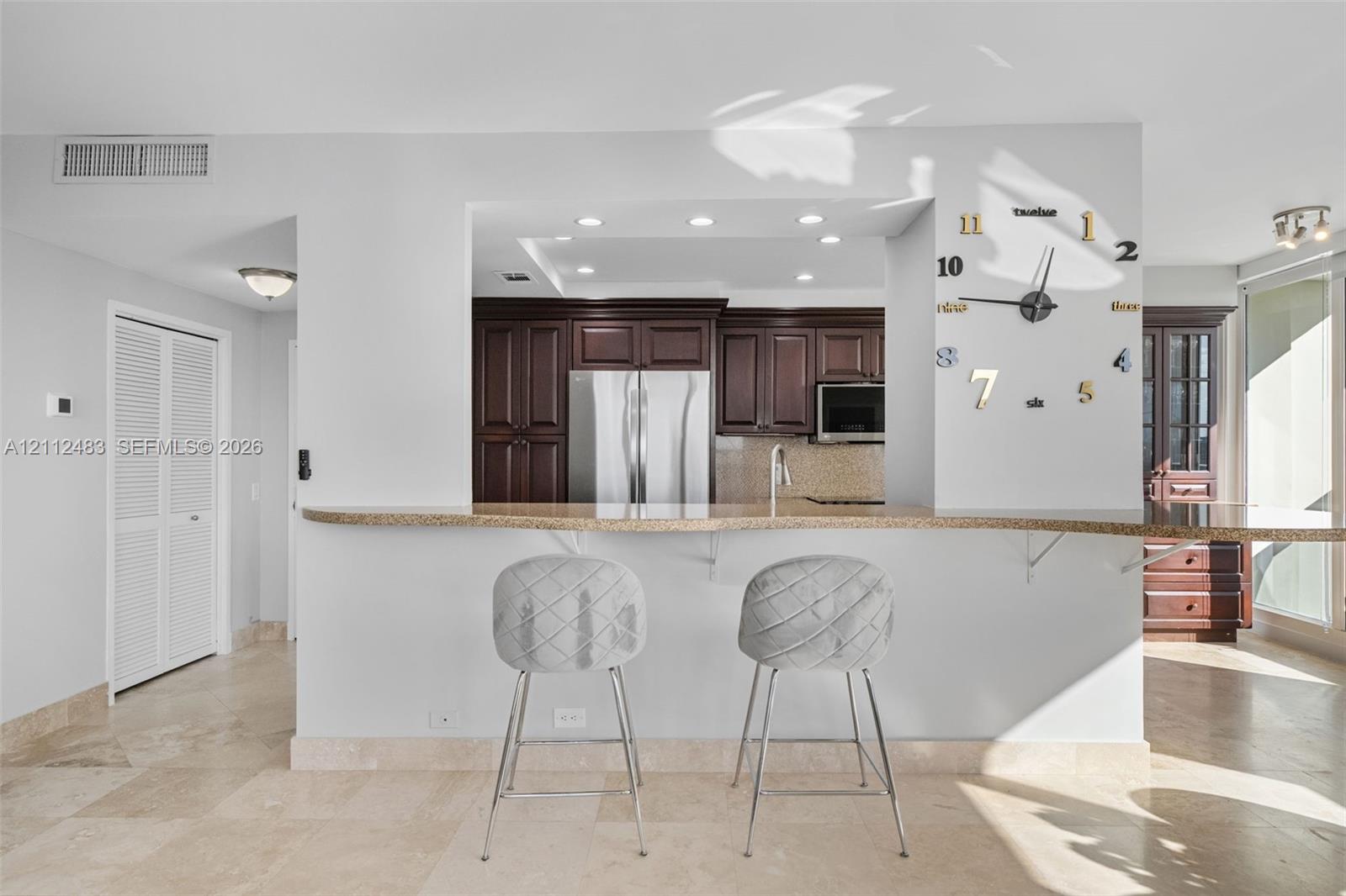 Kitchen pass-through window featuring a stone-topped breakfast bar, dark wood cabinetry, stainless steel appliances, recessed ceiling lighting, and tile flooring