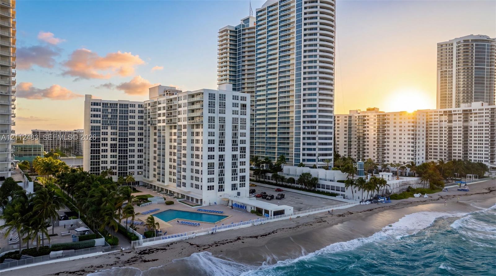 High-rise residential building featuring expansive glass curtain walls, private balconies, an on-site swimming pool, and direct oceanfront positioning