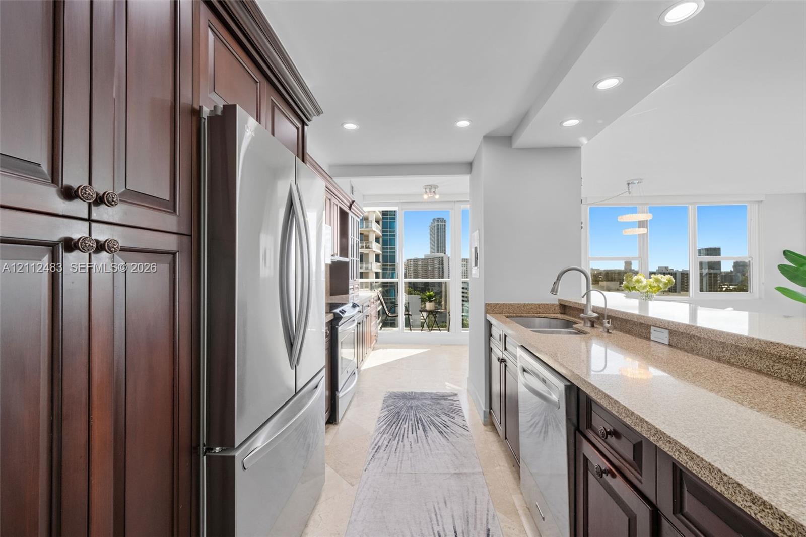 Kitchen featuring dark wood cabinetry, stainless steel appliances, stone countertops, recessed lighting, and large windows with urban scenery