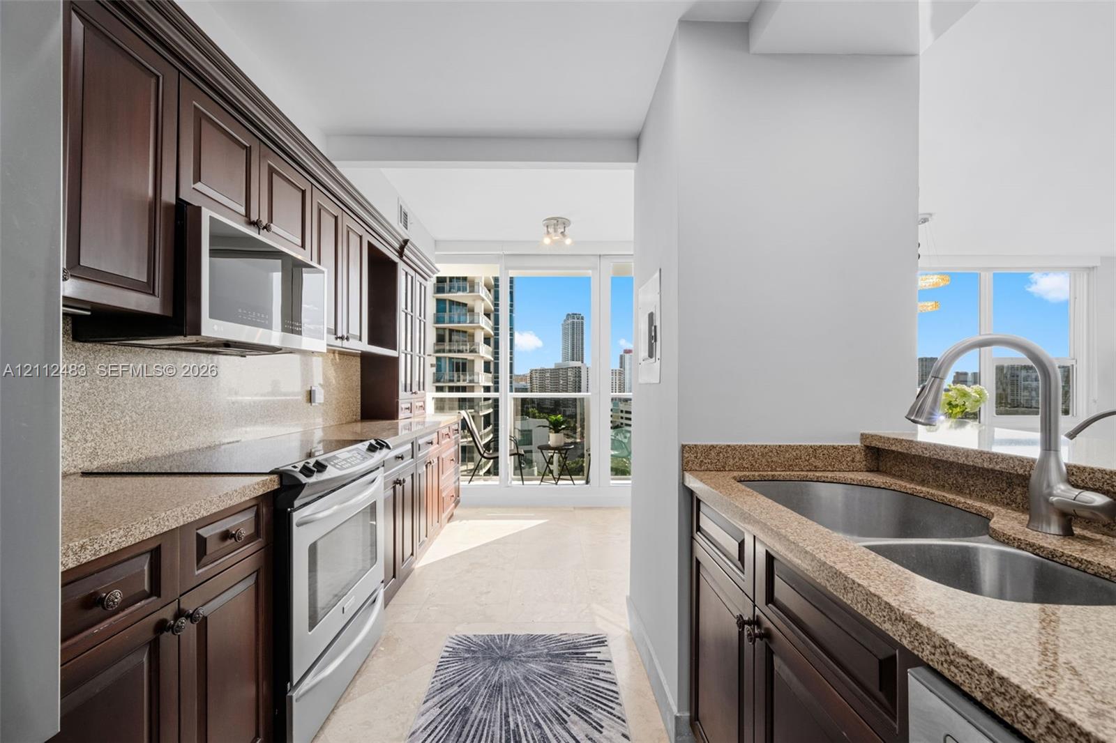 Kitchen featuring dark wood cabinetry, stone countertops, stainless steel appliances, a double-basin undermount sink with a gooseneck faucet, and floor-to-ceiling windows