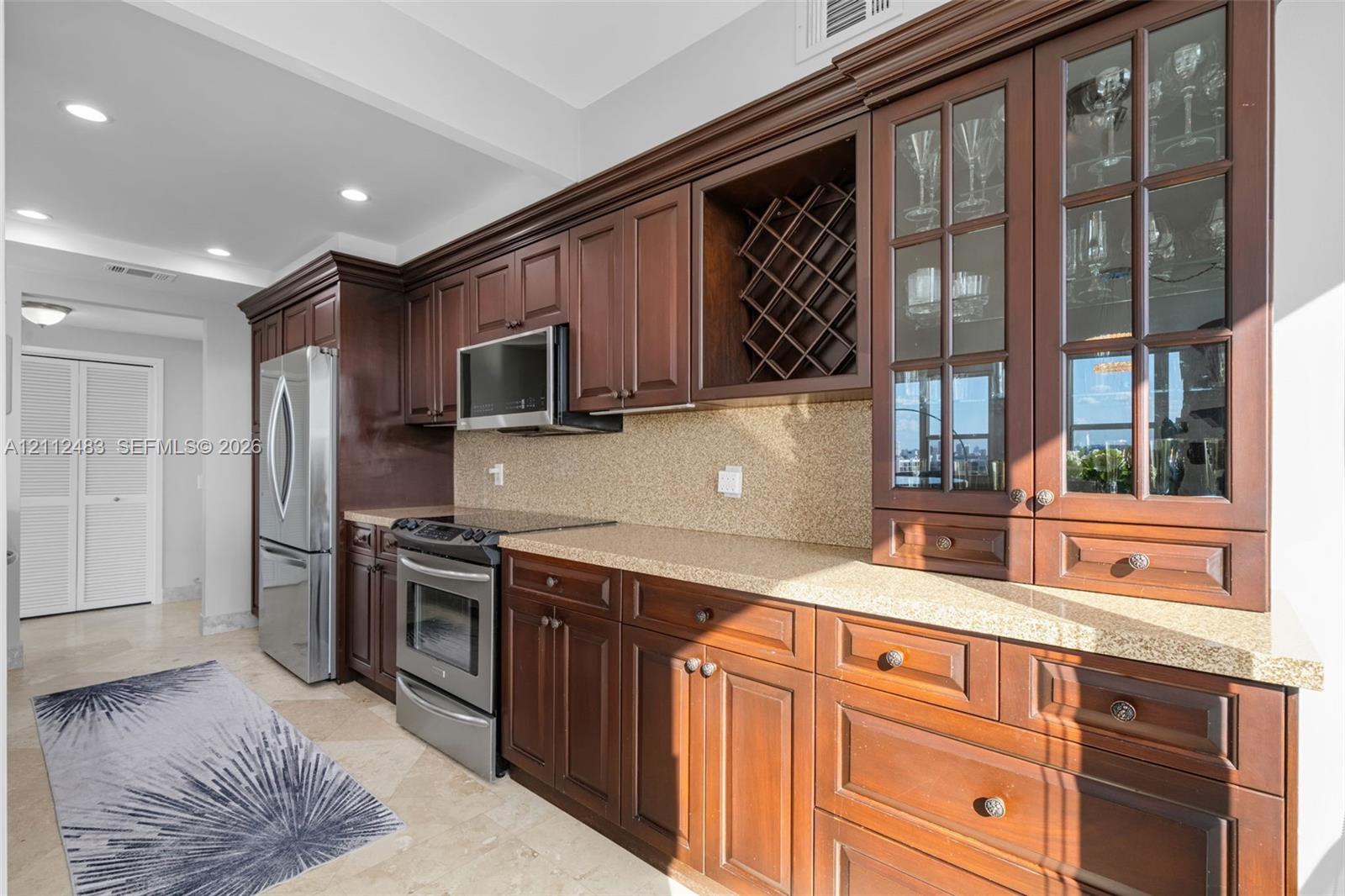 Kitchen featuring cherry-finish cabinetry, stone-texture countertops, stainless steel appliances, built-in wine storage, and glass-paneled display cabinets