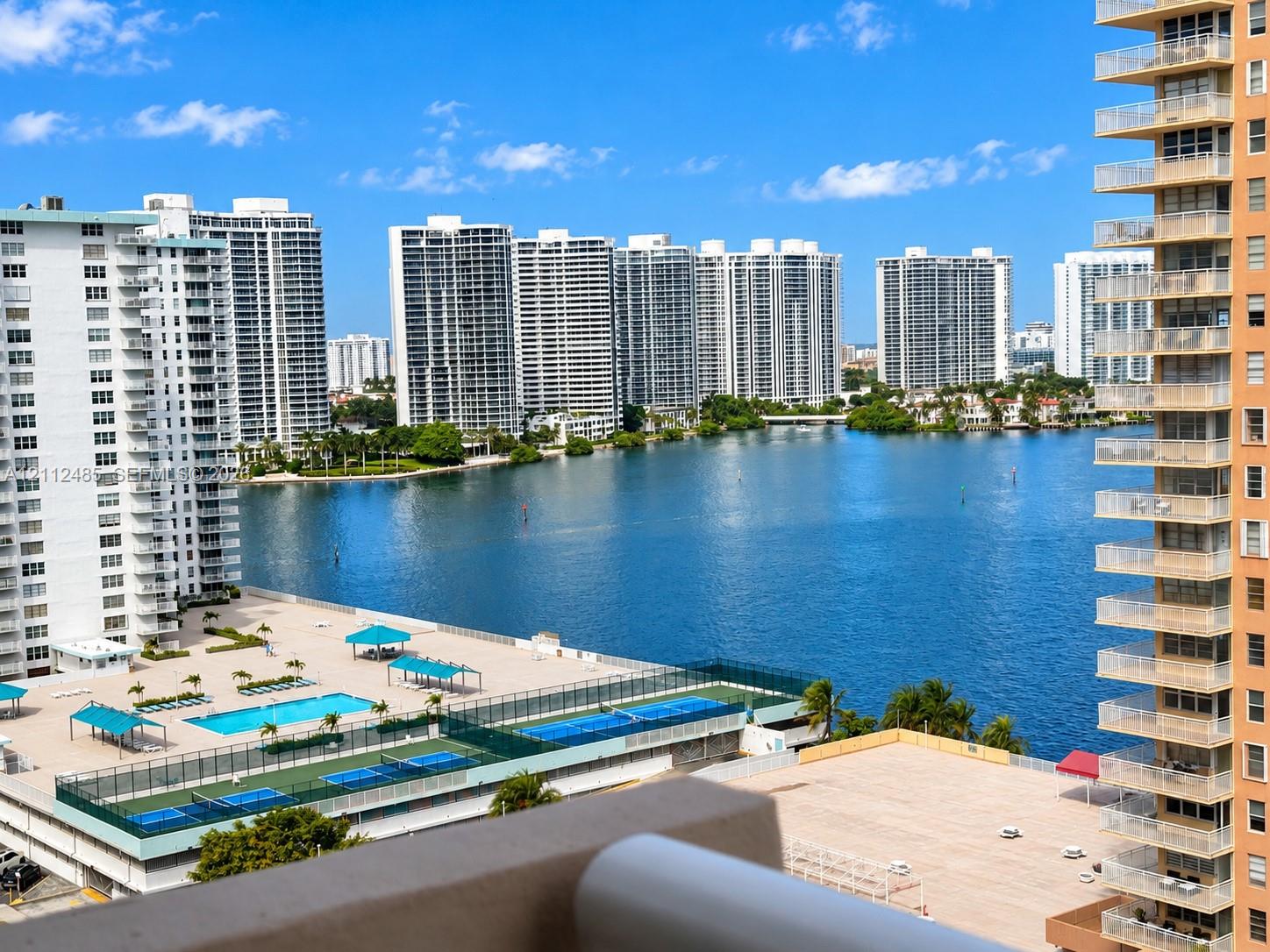 Elevated balcony overview featuring an outdoor swimming pool, fenced tennis courts, and expansive water frontage