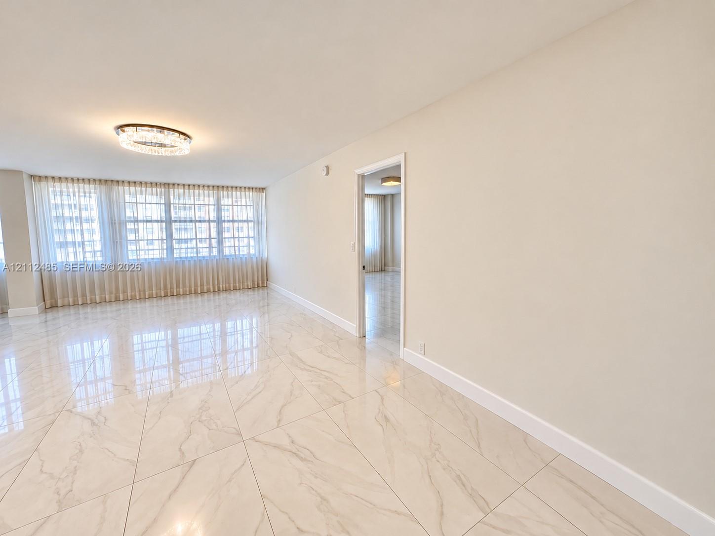 Large-format polished flooring with veined detailing, floor-to-ceiling windows with integrated drapery, and a contemporary circular flush-mount light fixture
