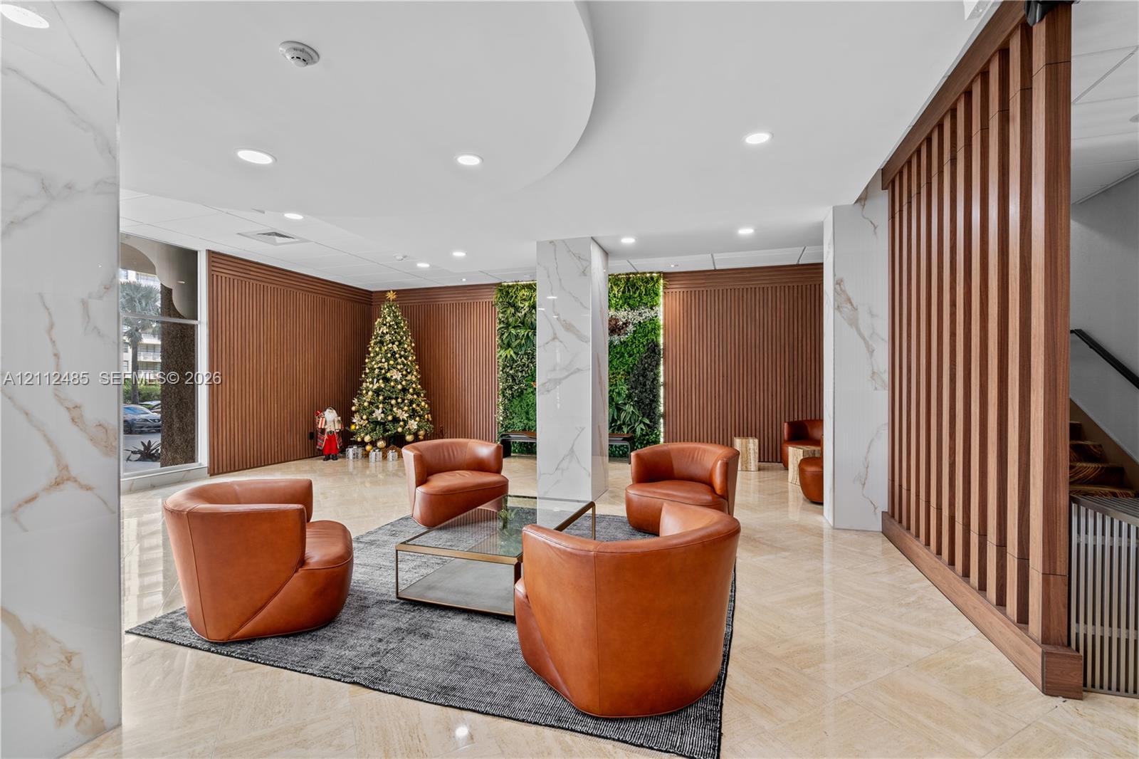 Lobby area featuring large-format tile flooring, vertical wood-slat wall paneling, stone-finished structural columns, and a floor-to-ceiling interior plant wall
