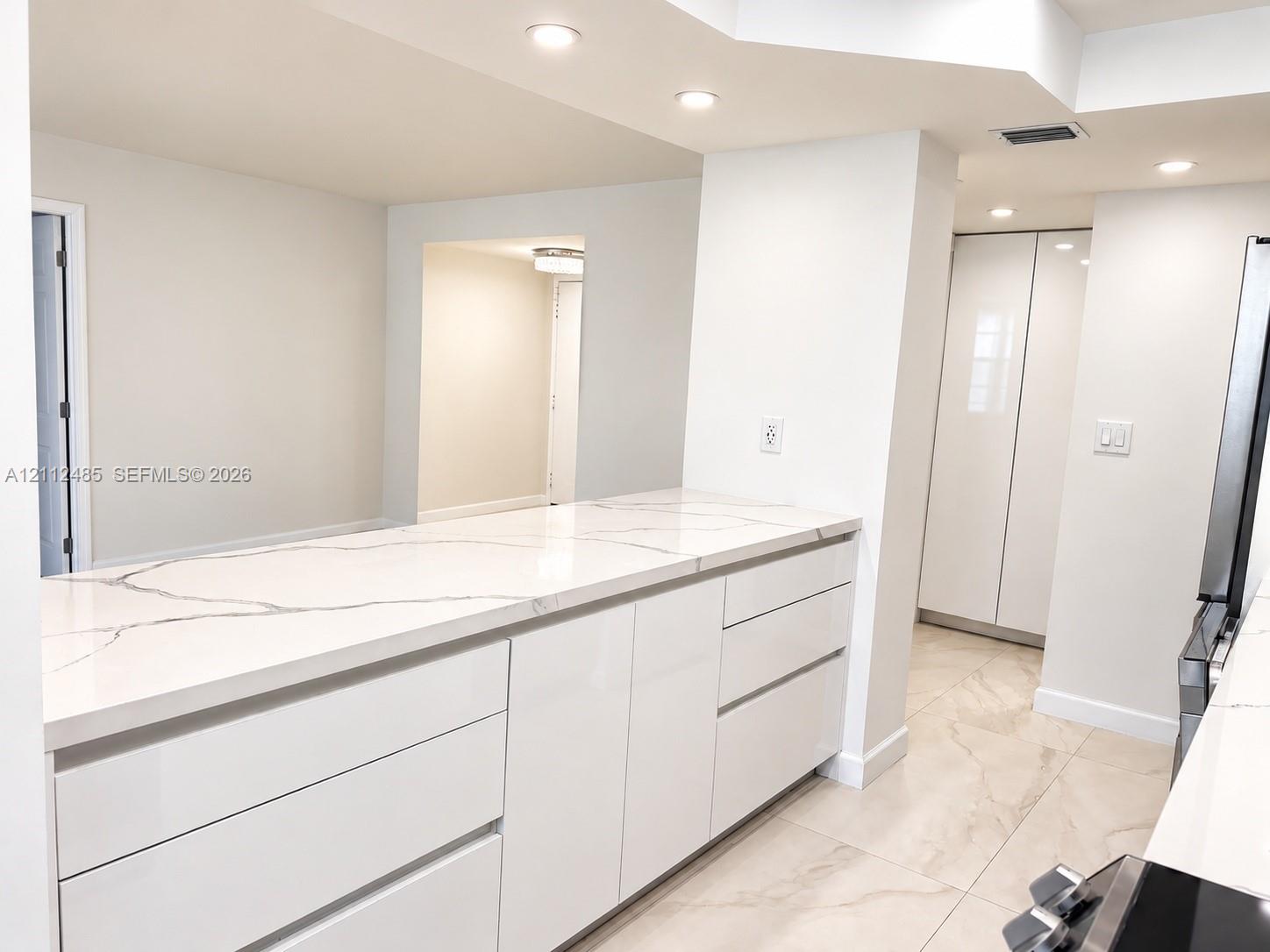 Kitchen featuring high-gloss cabinetry, stone-finish countertops, tile flooring, and integrated recessed lighting Kitchen featuring high-gloss cabinetry, stone-finish countertops, tile flooring, and integrated recessed lighting
