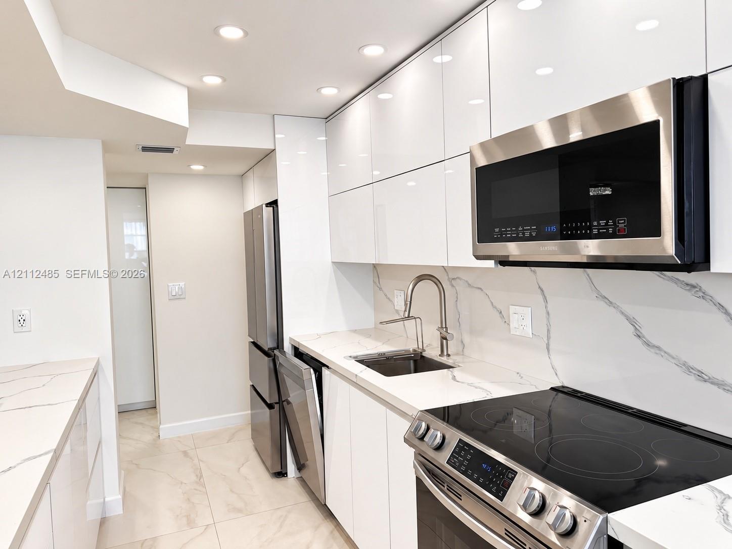 Kitchen featuring high-gloss cabinetry, veined stone-surface countertops, full-height matching backsplash, integrated stainless steel appliances, and recessed ceiling lighting Kitchen featuring high-gloss cabinetry, veined stone-surface countertops, full-height matching backsplash, integrated stainless steel appliances, and recessed ceiling lighting