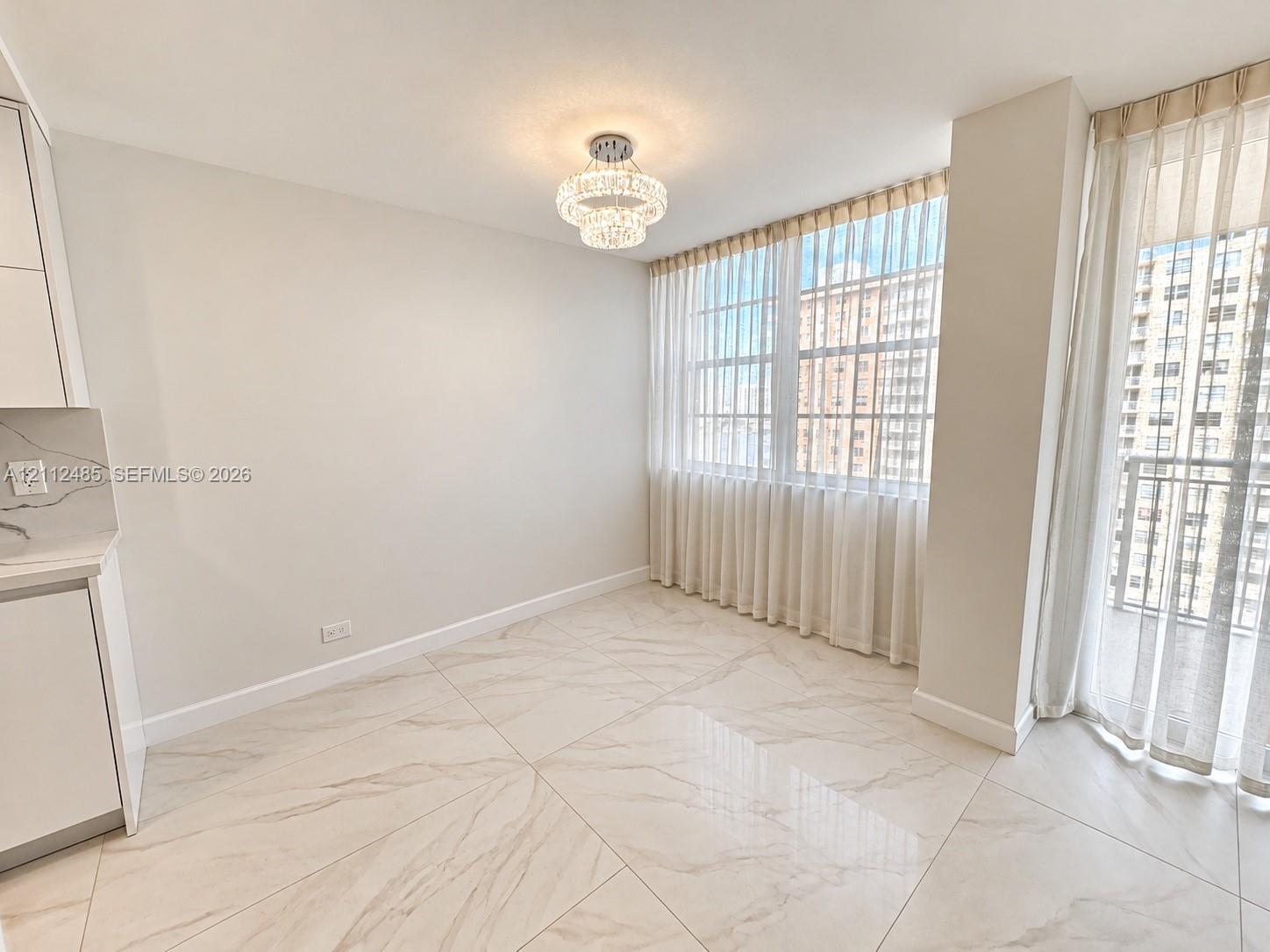 Large-format tile flooring, crystal-accented tiered chandelier, floor-to-ceiling windows, and kitchen cabinetry with quartz-patterned countertops Large-format tile flooring, crystal-accented tiered chandelier, floor-to-ceiling windows, and kitchen cabinetry with quartz-patterned countertops