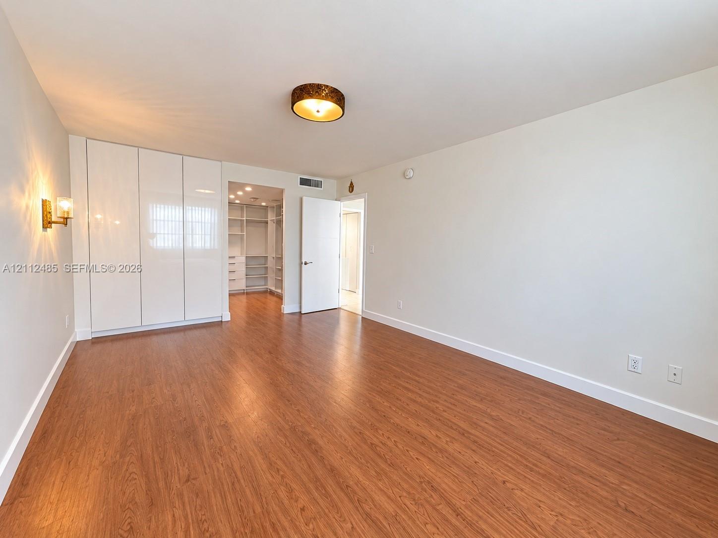 Wood-finish flooring, full-height white cabinetry with smooth-finish doors, built-in closet shelving system, brass-tone wall-mounted lighting, and a drum-style ceiling light fixture