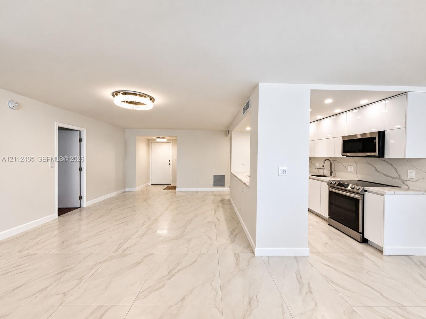 Open-concept floor plan featuring large-format stone-finish flooring, high-gloss white cabinetry, integrated stainless steel appliances, and minimalist ceiling-mounted lighting Open-concept floor plan featuring large-format stone-finish flooring, high-gloss white cabinetry, integrated stainless steel appliances, and minimalist ceiling-mounted lighting