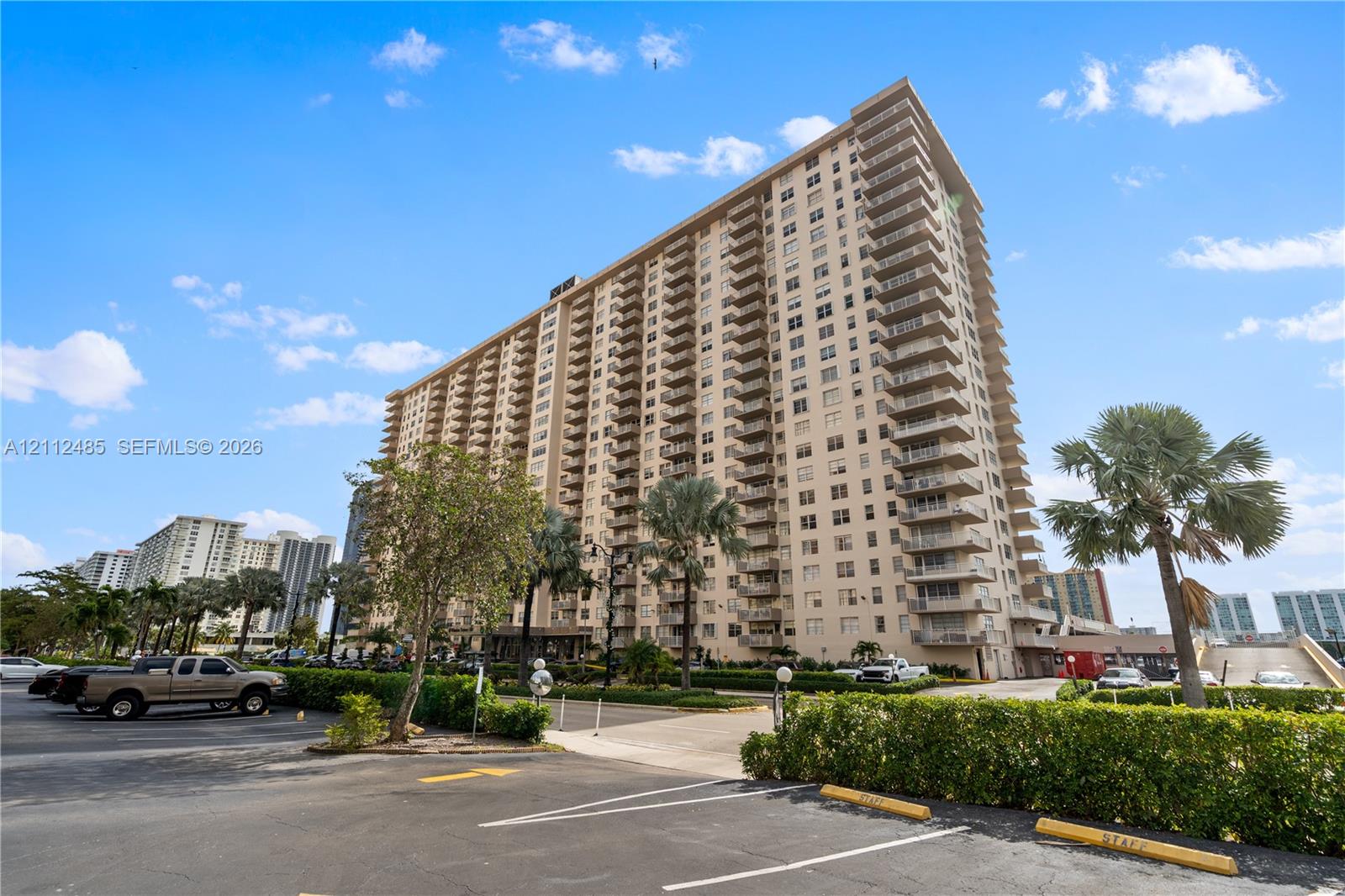 High-rise residential exterior featuring expansive concrete balconies, structured architectural facade, and paved parking area with established landscape greenery