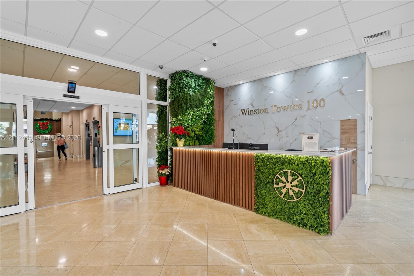 Lobby area featuring large-format tile flooring, a custom reception desk with slatted wood detailing, integrated greenery wall accents, and a back-lit feature wall