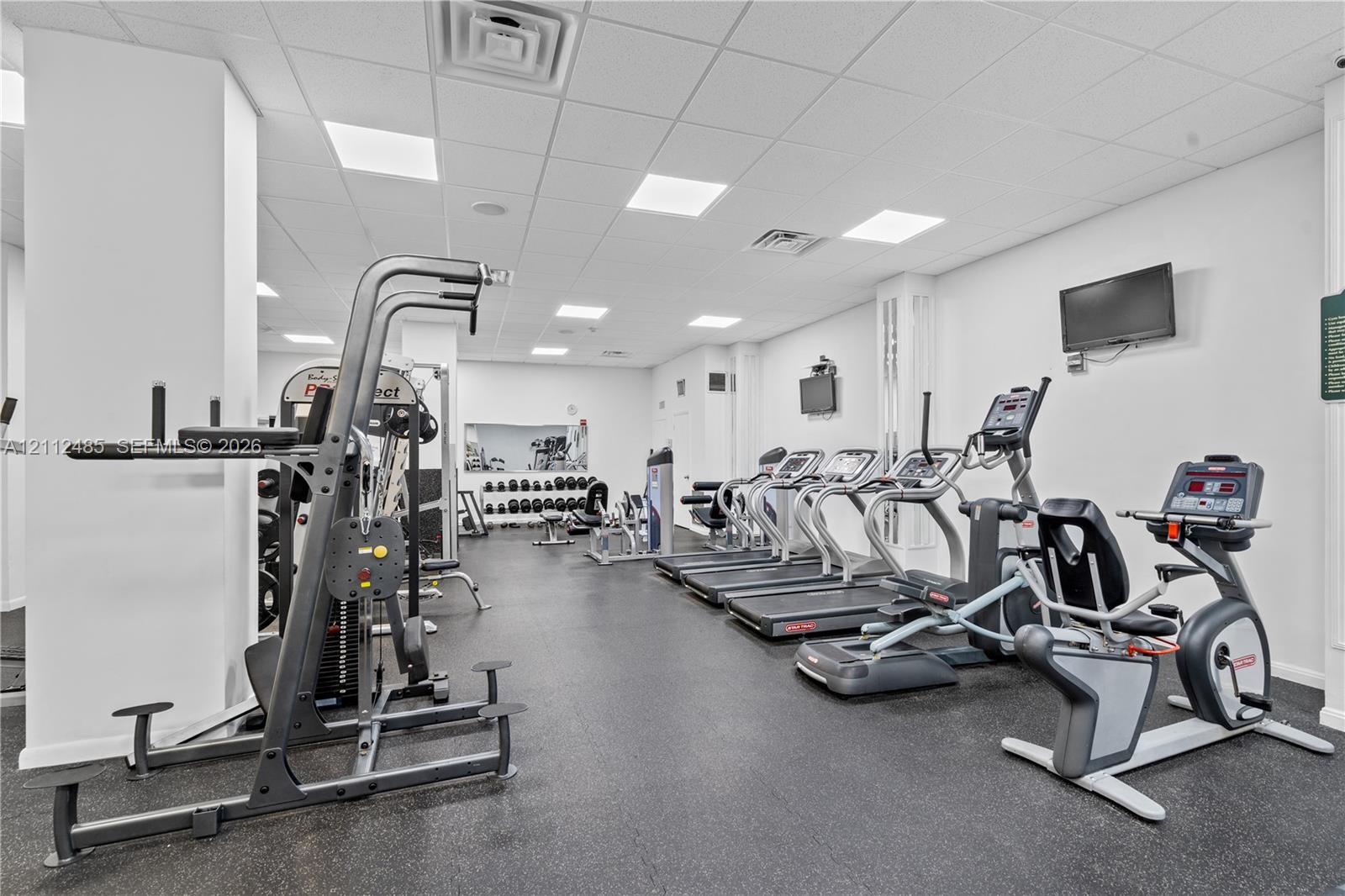 Fitness center featuring a drop ceiling with recessed lighting, rubberized flooring, and wall-mounted televisions