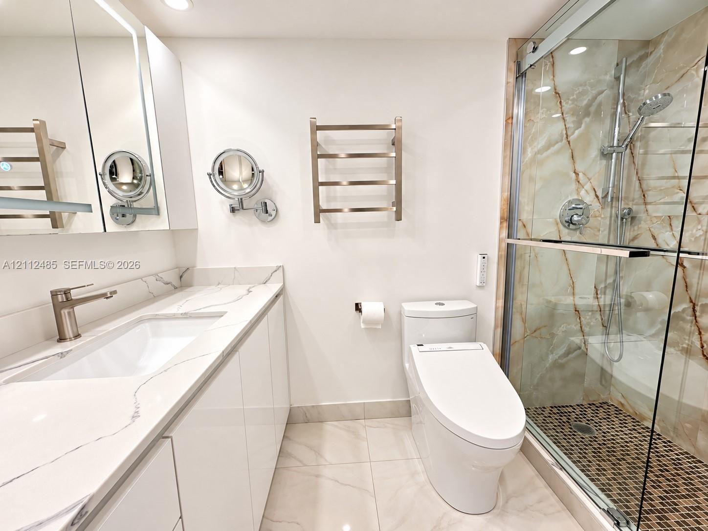Bathroom featuring a vanity with a white countertop, walk-in shower with glass enclosure and stone-patterned wall tile, wall-mounted heated towel rack, and polished nickel hardware