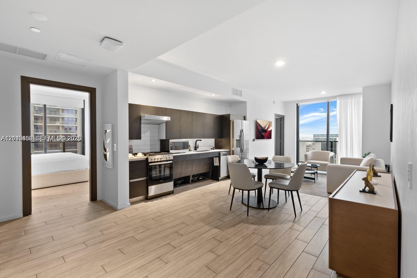 Open-concept interior featuring wood-finish tile flooring, custom flat-panel cabinetry, stainless steel kitchen appliances, and floor-to-ceiling windows