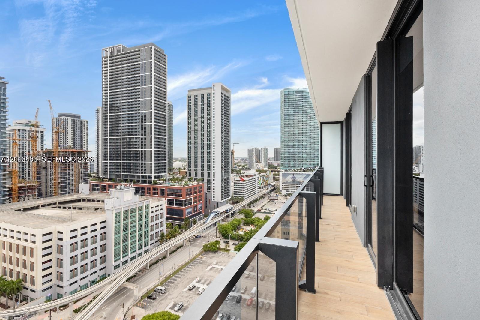 Covered balcony featuring wood-finish flooring, glass panel railings, and metal structural framing Covered balcony featuring wood-finish flooring, glass panel railings, and metal structural framing