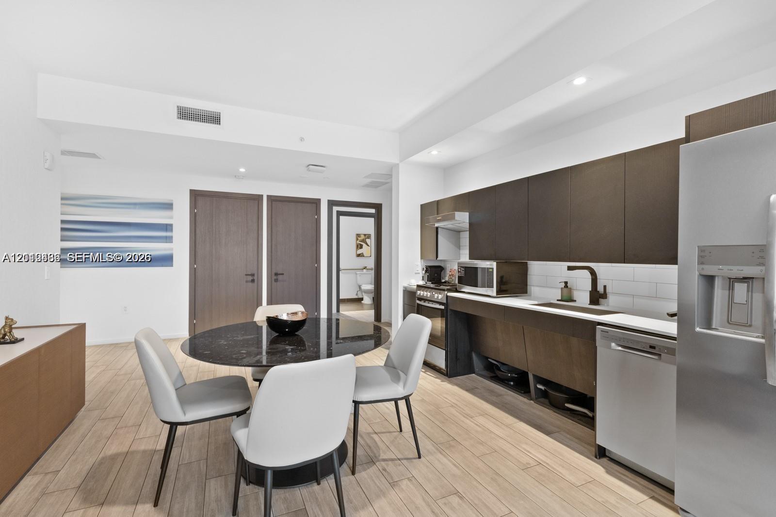 Contemporary kitchen featuring flat-panel cabinetry, stainless steel appliances, subway tile backsplash, recessed lighting, and wood-finish flooring Contemporary kitchen featuring flat-panel cabinetry, stainless steel appliances, subway tile backsplash, recessed lighting, and wood-finish flooring