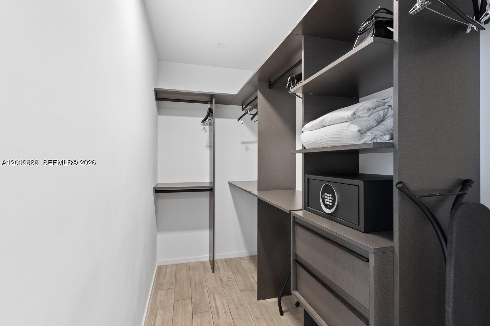 Custom closet system featuring dark wood-finish cabinetry, integrated shelving, hanging rods, and two soft-close drawers, complemented by wood-finish flooring Custom closet system featuring dark wood-finish cabinetry, integrated shelving, hanging rods, and two soft-close drawers, complemented by wood-finish flooring