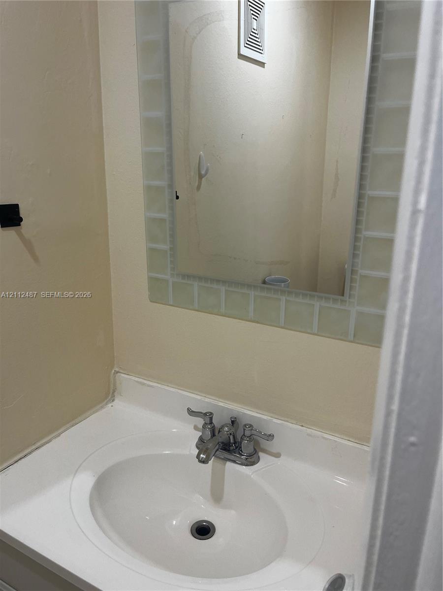 White vanity with an integrated sink basin and double-handle chrome faucet, accompanied by a wall-mounted mirror framed with square glass tile detailing White vanity with an integrated sink basin and double-handle chrome faucet, accompanied by a wall-mounted mirror framed with square glass tile detailing