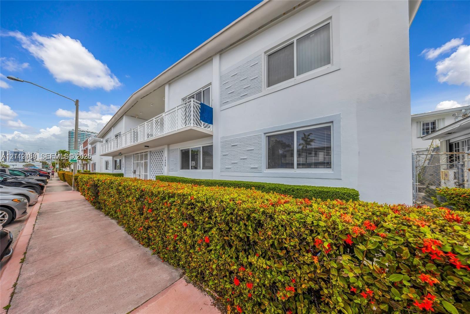 Exterior facade featuring white stucco finish, geometric decorative siding panels, sliding windows, and a railed second-story balcony