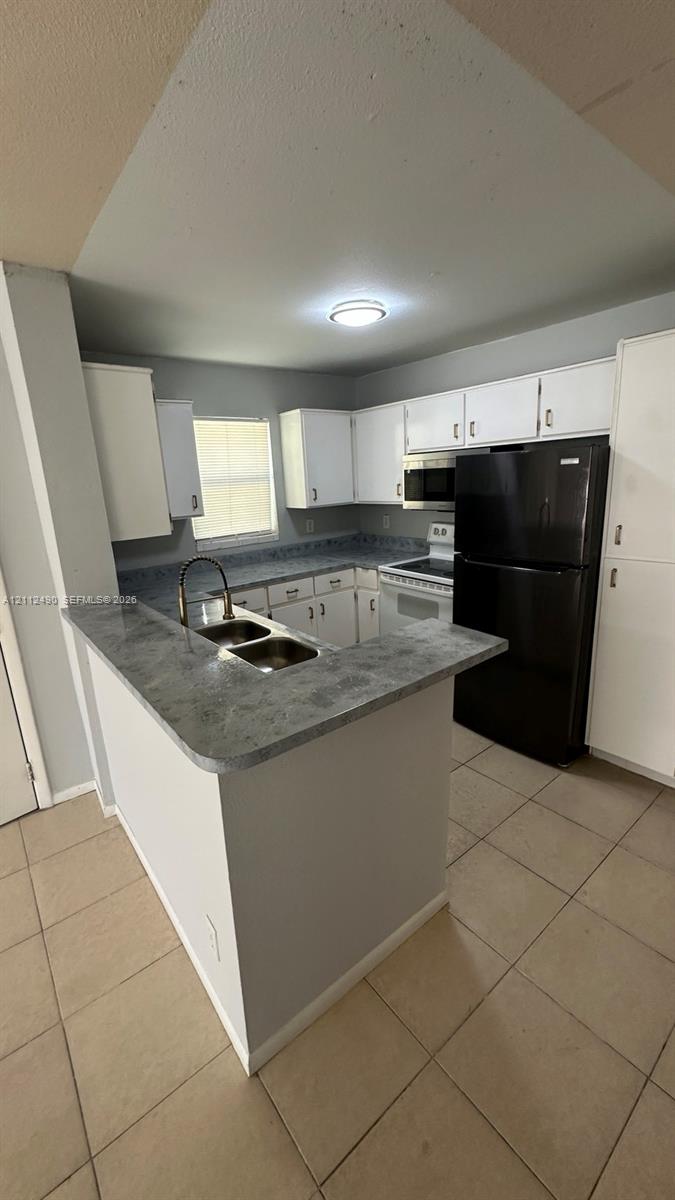 Kitchen featuring white cabinetry, solid-surface countertops, dual-basin stainless steel sink, tiled flooring, and built-in appliances