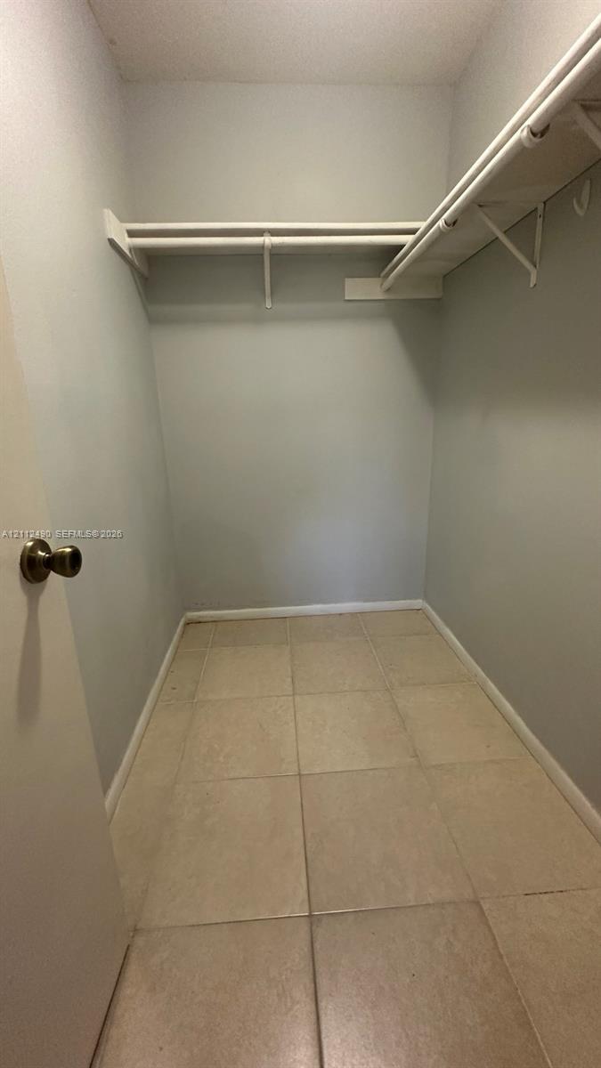 Walk-in storage space featuring tiled flooring and upper built-in shelving with integrated rods