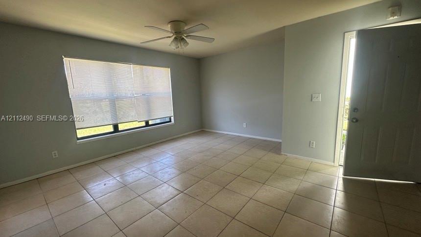 Neutral-toned interior featuring large-format tile flooring, a ceiling fan with integrated lighting, and a window with horizontal blinds