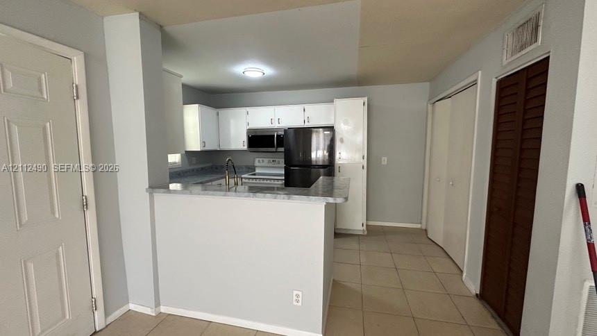 Kitchen featuring white cabinetry, stone-patterned countertops, a peninsula breakfast bar, dark-finish appliances, and tile flooring
