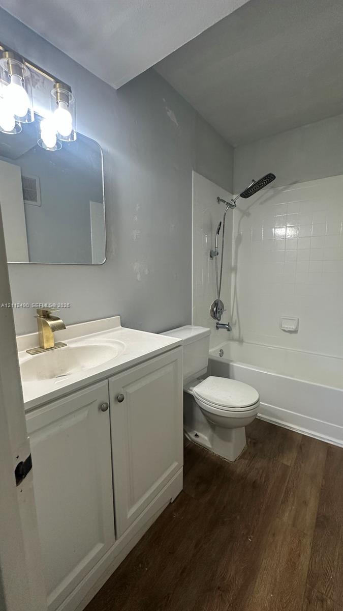 Bathroom featuring a white vanity cabinet, wood-finish flooring, gold-toned faucet, rectangular mirror with rounded corners, and a white shower-tub combination