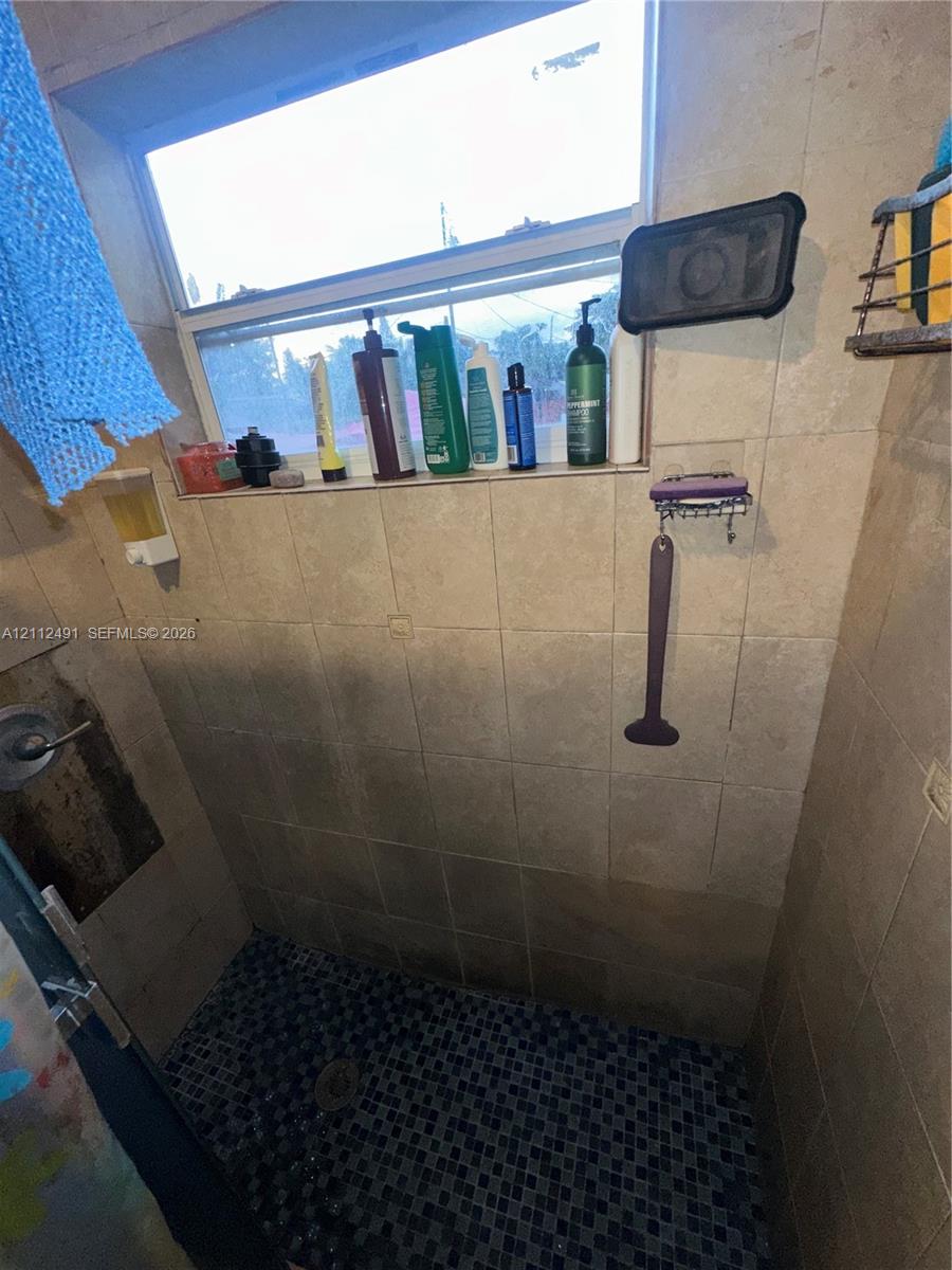 Shower enclosure featuring large-format neutral-toned wall tiles, dark mosaic floor tiling, and an integrated horizontal tile shelf