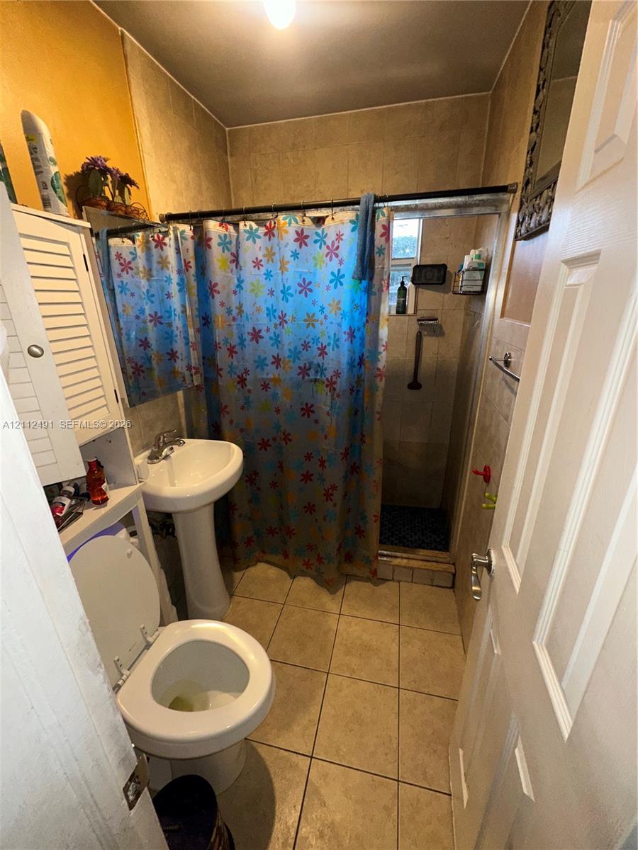 Bathroom featuring large-format tile flooring, pedestal sink, and tiled shower surround with a metal rod fixture