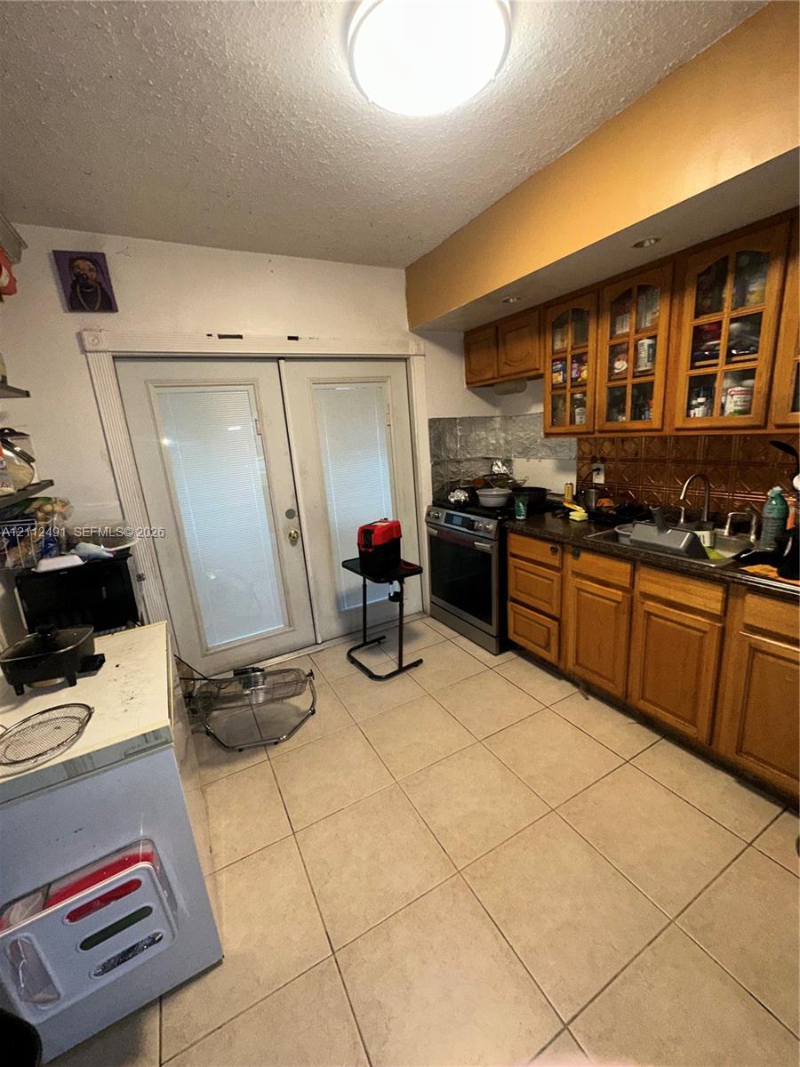 Kitchen featuring wood cabinetry with glass-panel upper doors, tile flooring, stainless steel range, and double glass-paneled exterior doors