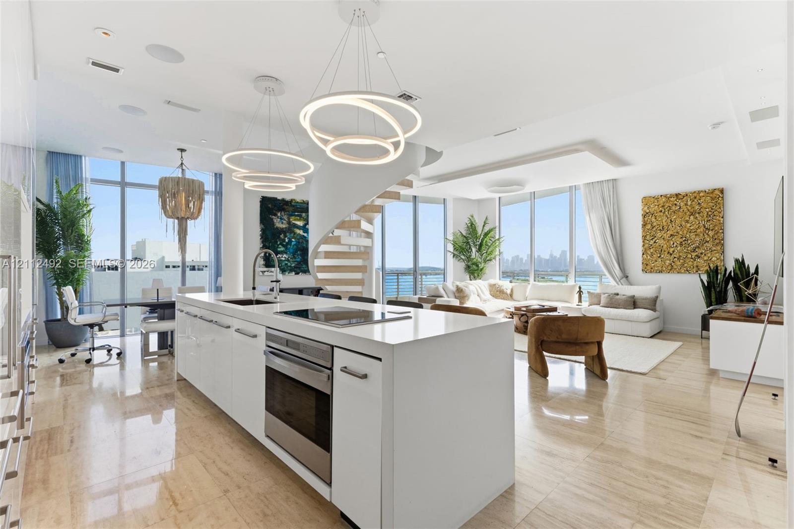 Open concept kitchen featuring a stone-topped island, stainless steel built-in oven, contemporary ring chandeliers, polished stone flooring, and a structural spiral staircase