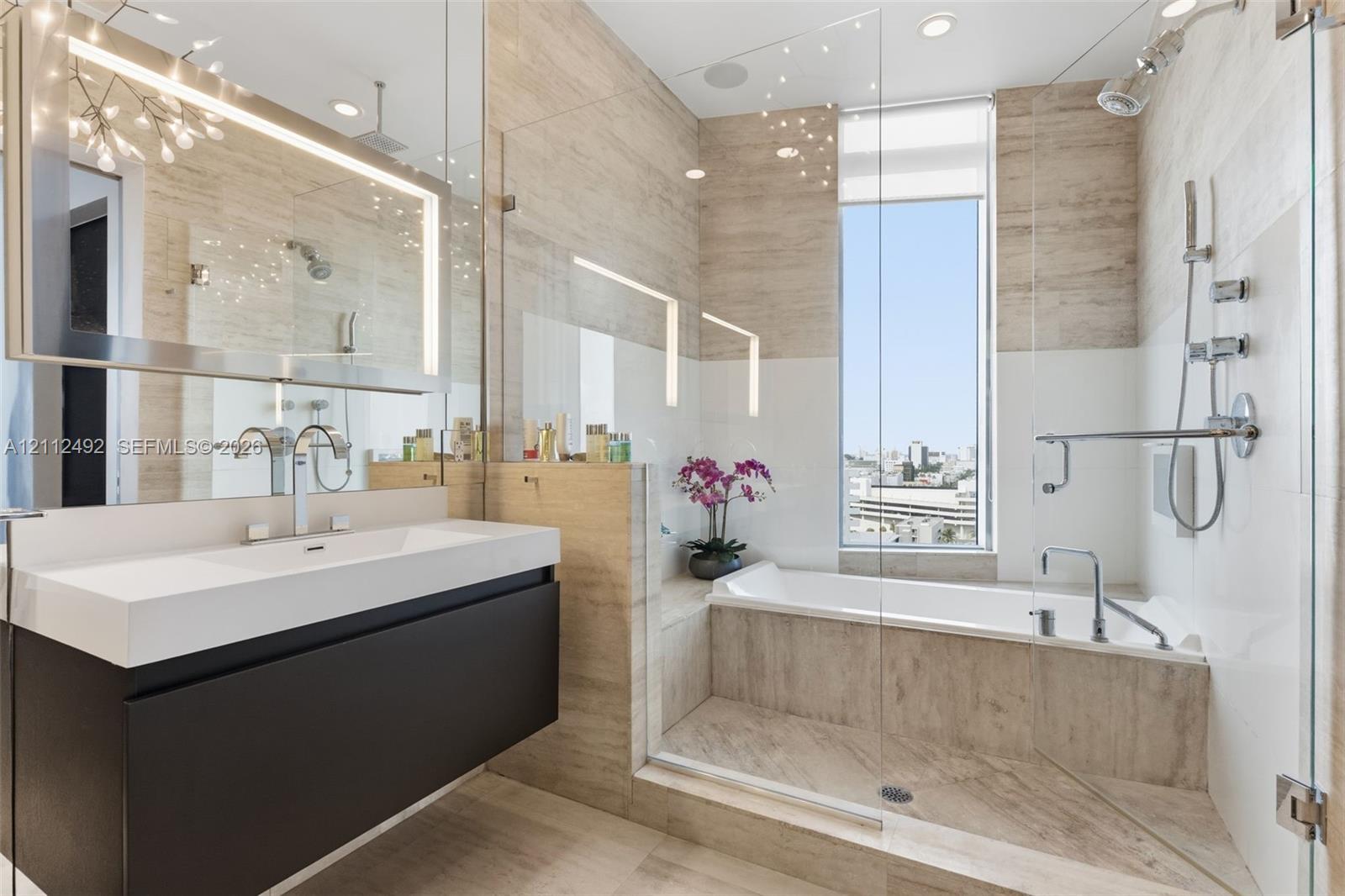 Bathroom featuring a wall-mounted floating vanity with integrated rectangular sink, large-format tiled wall surfacing, glass-enclosed shower and tub combination, and polished chrome fixtures