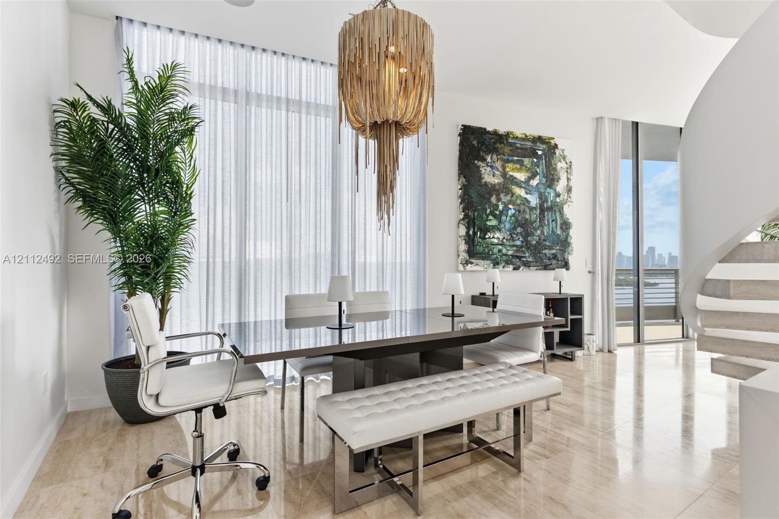 Full-height windows, natural stone flooring, statement tiered chandelier, and a curved architectural staircase