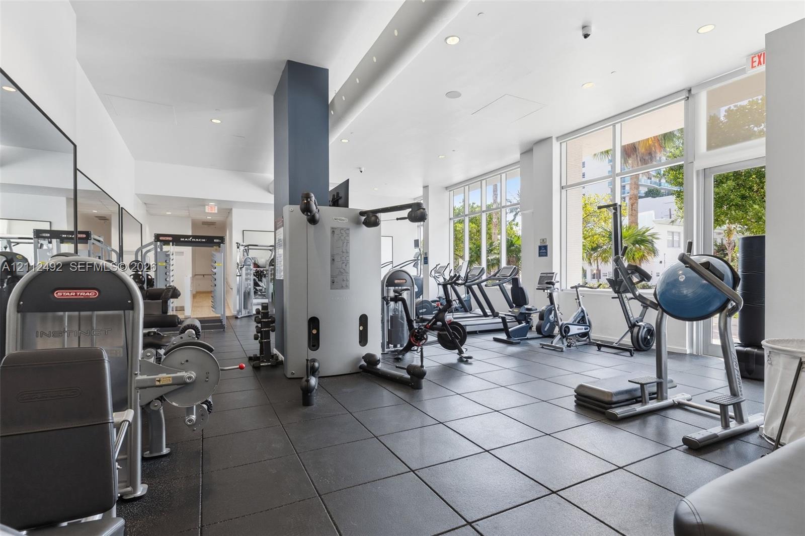 Fitness center featuring large-format floor tiling, recessed lighting, floor-to-ceiling windows, and mirrored wall surfaces