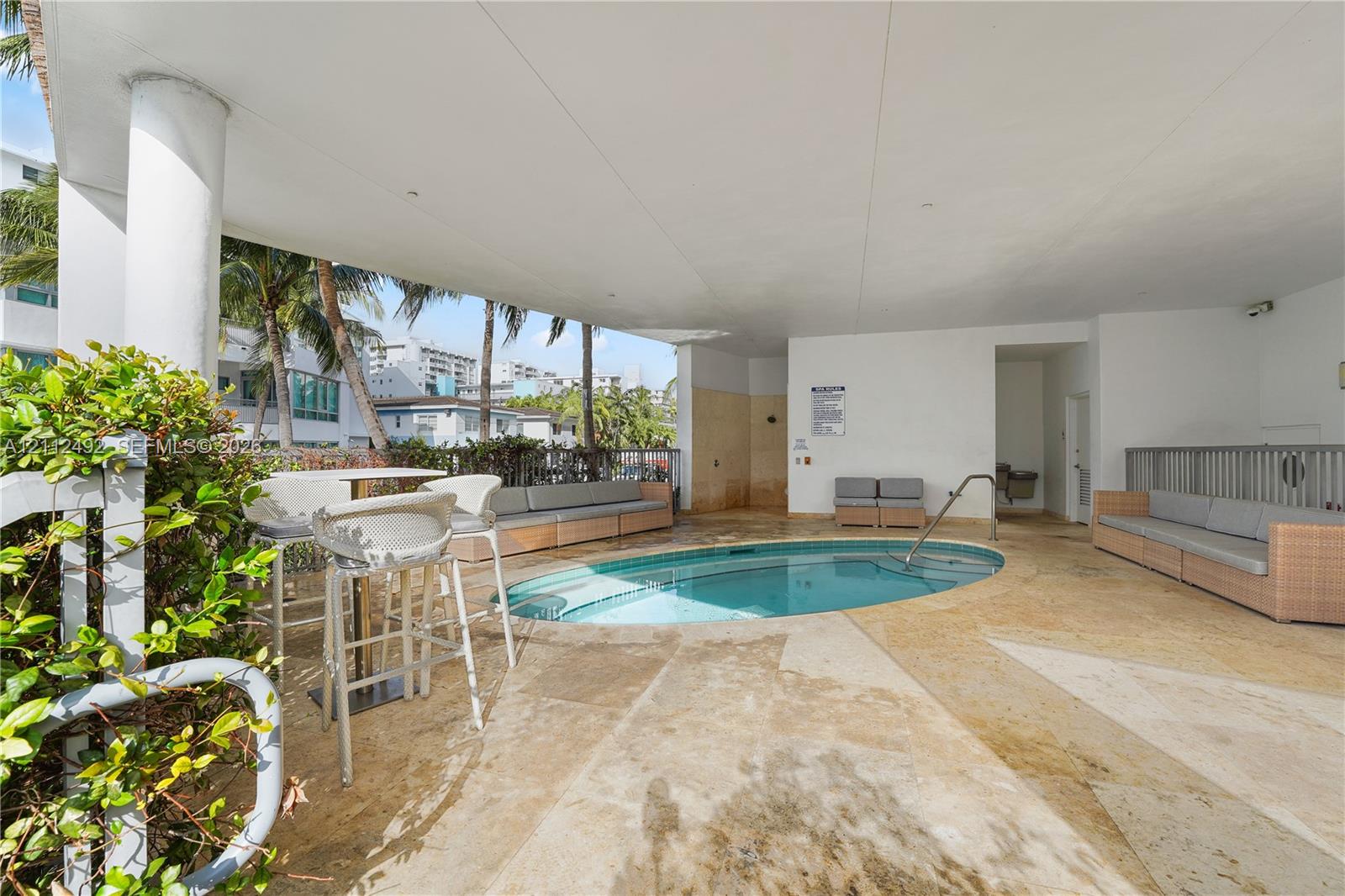 Covered outdoor patio featuring natural stone flooring, a recessed oval pool with metal handrails, and structural support columns