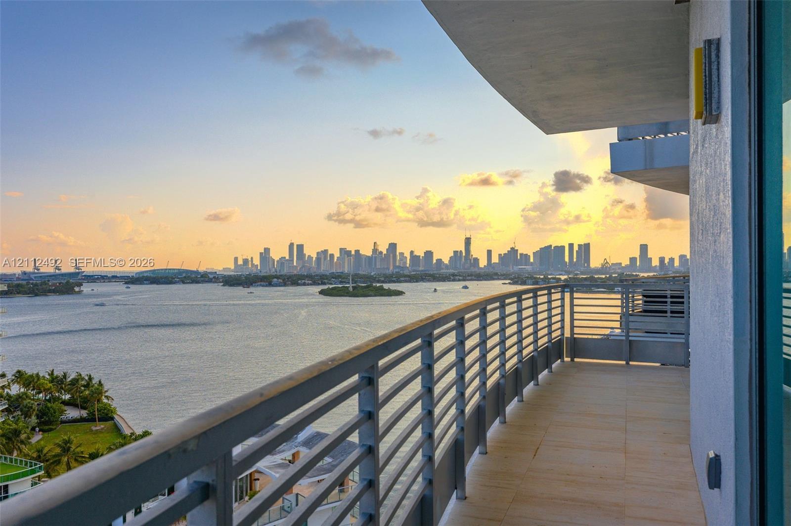 Covered balcony featuring tile flooring and horizontal metal railings, overlooking the waterfront and cityscape