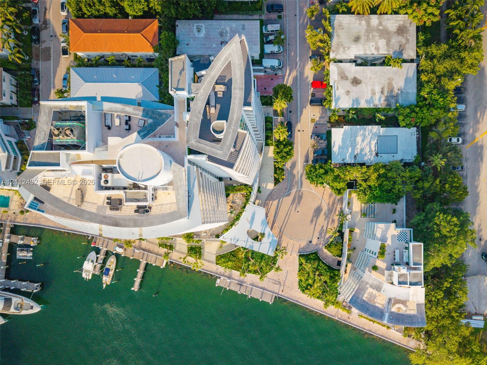 Aerial perspective of a multi-level waterfront estate featuring a private deep-water dock, extensive rooftop terrace space, and hardscaped circular motor court