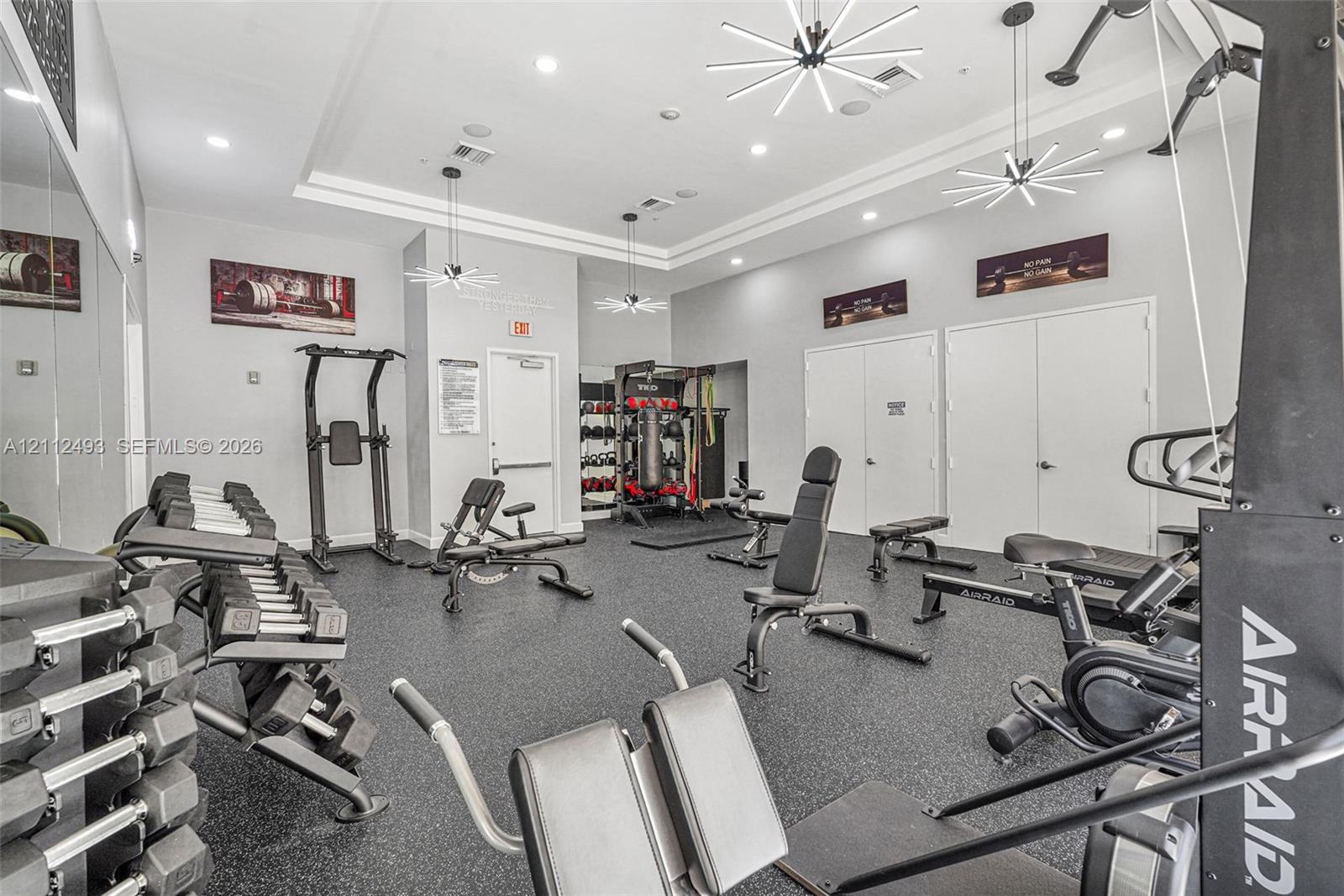 Fitness center featuring rubberized flooring, recessed lighting, modern tiered chandeliers, and wall-to-wall mirrors
