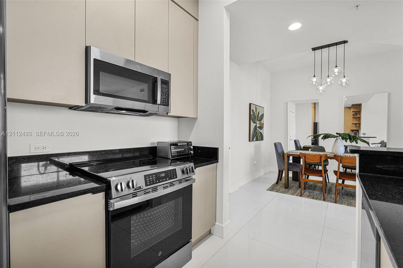 Kitchen featuring light-finish cabinetry, black stone countertops, stainless steel appliances, and large-format tile flooring